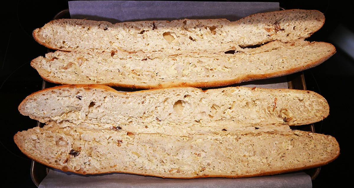 Image if two garlic baguettes on a cookie sheet with parchment paper on the cookie sheet before baking.