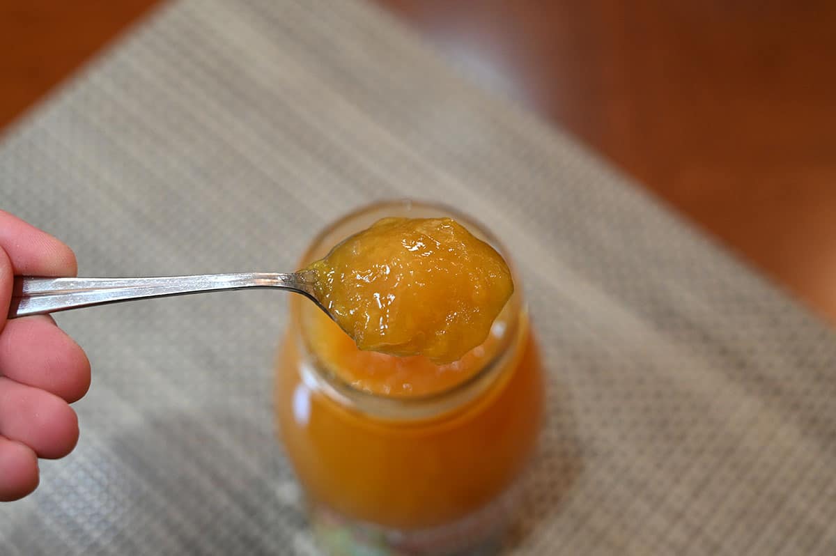 Image of a spoonful of peach spread from the jar. 