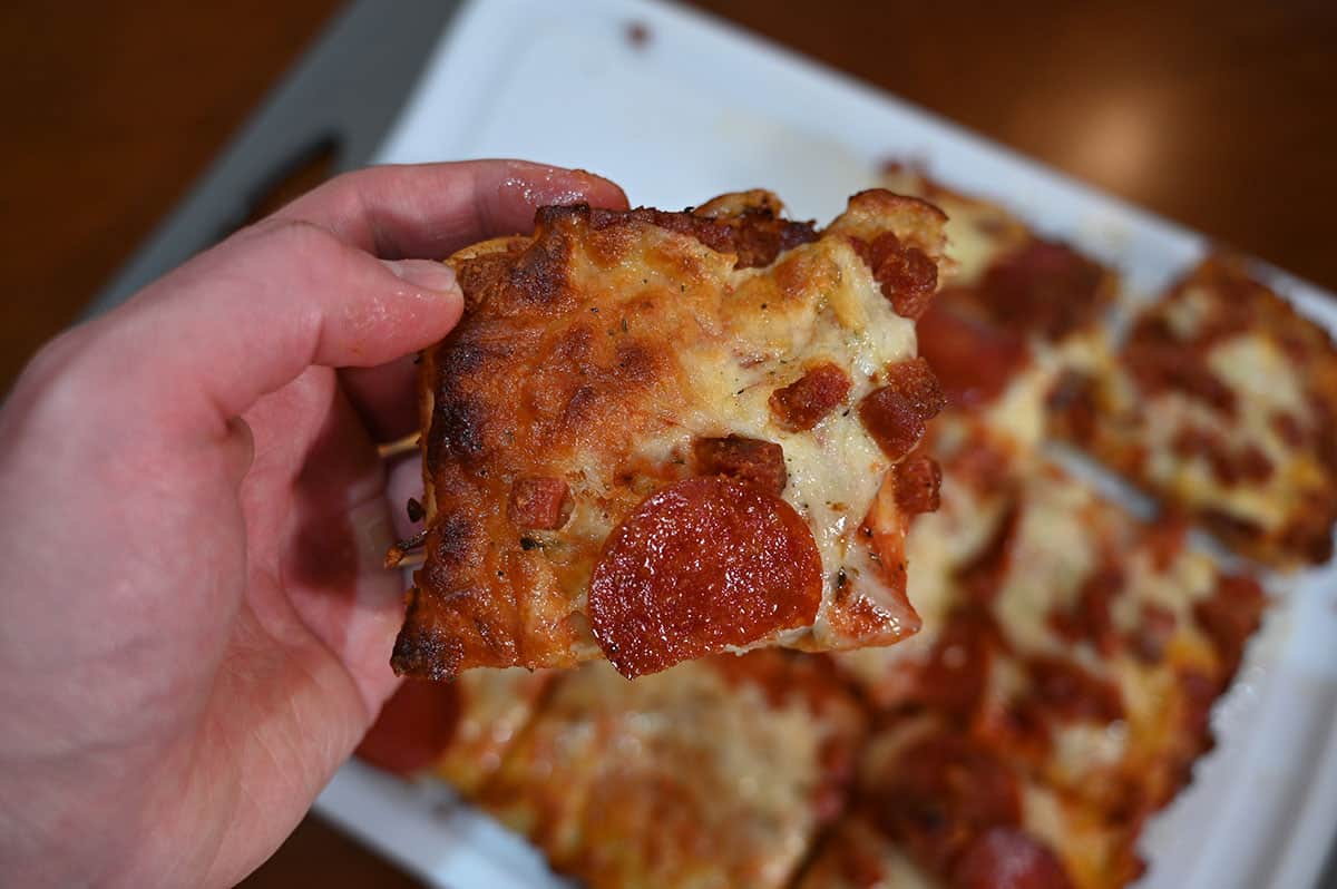 Closeup image of a hand holding one slice of pizza.