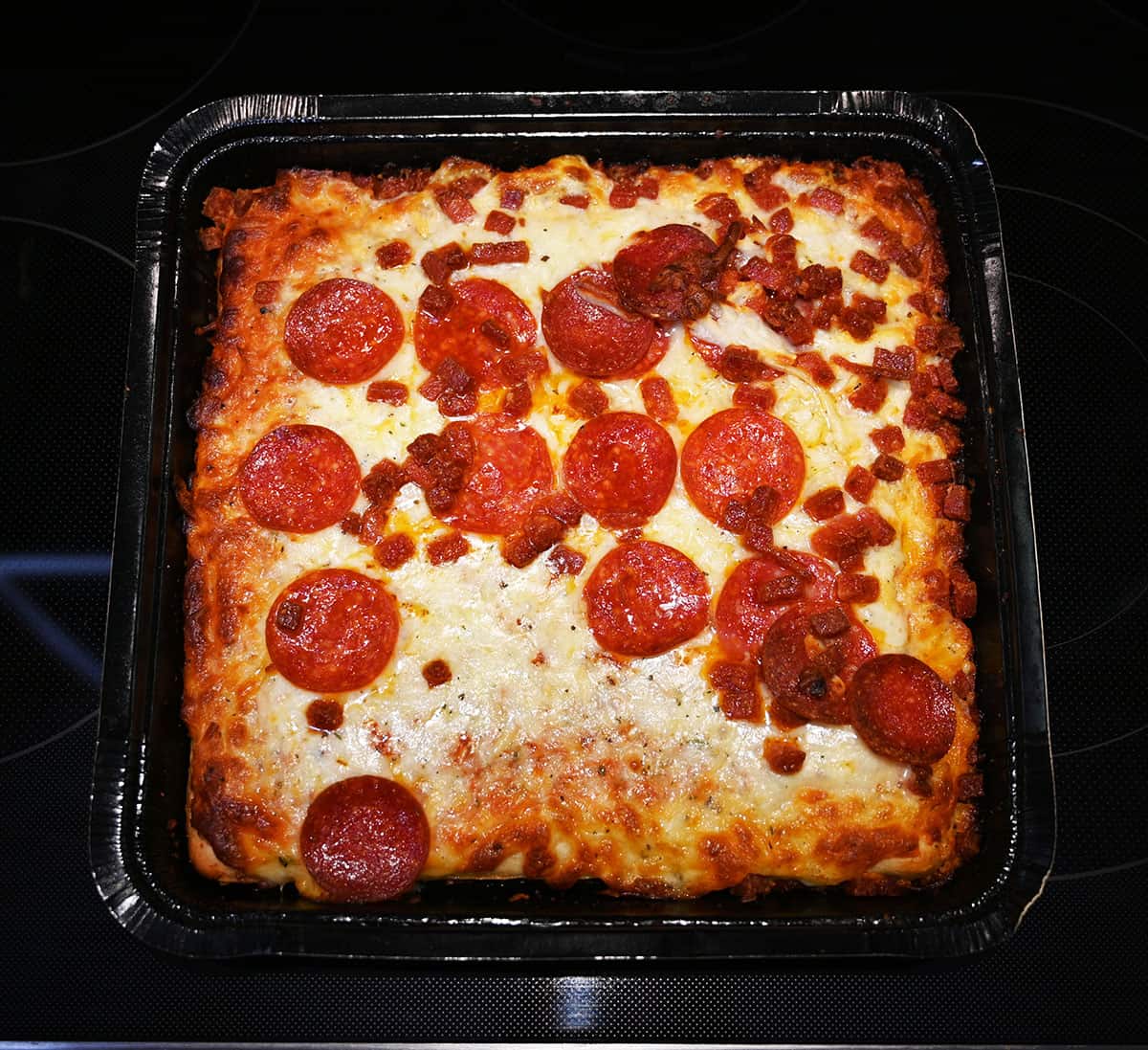 Top down image of the pizza cooked, on an oven stovetop, cooling.