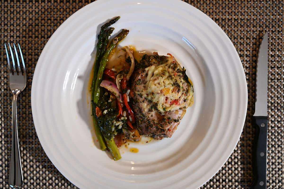 Top down image of the pork tenderloin cooked and served on a white plate, on a placemat with cutlery beside it.