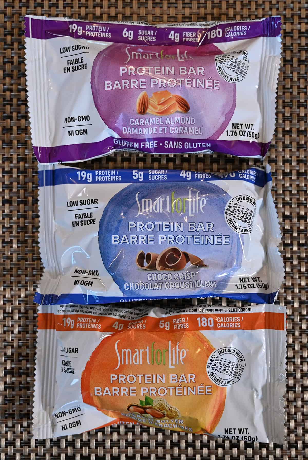 Closeup image of all three flavors of the protein bars in their packaging on a placemat.