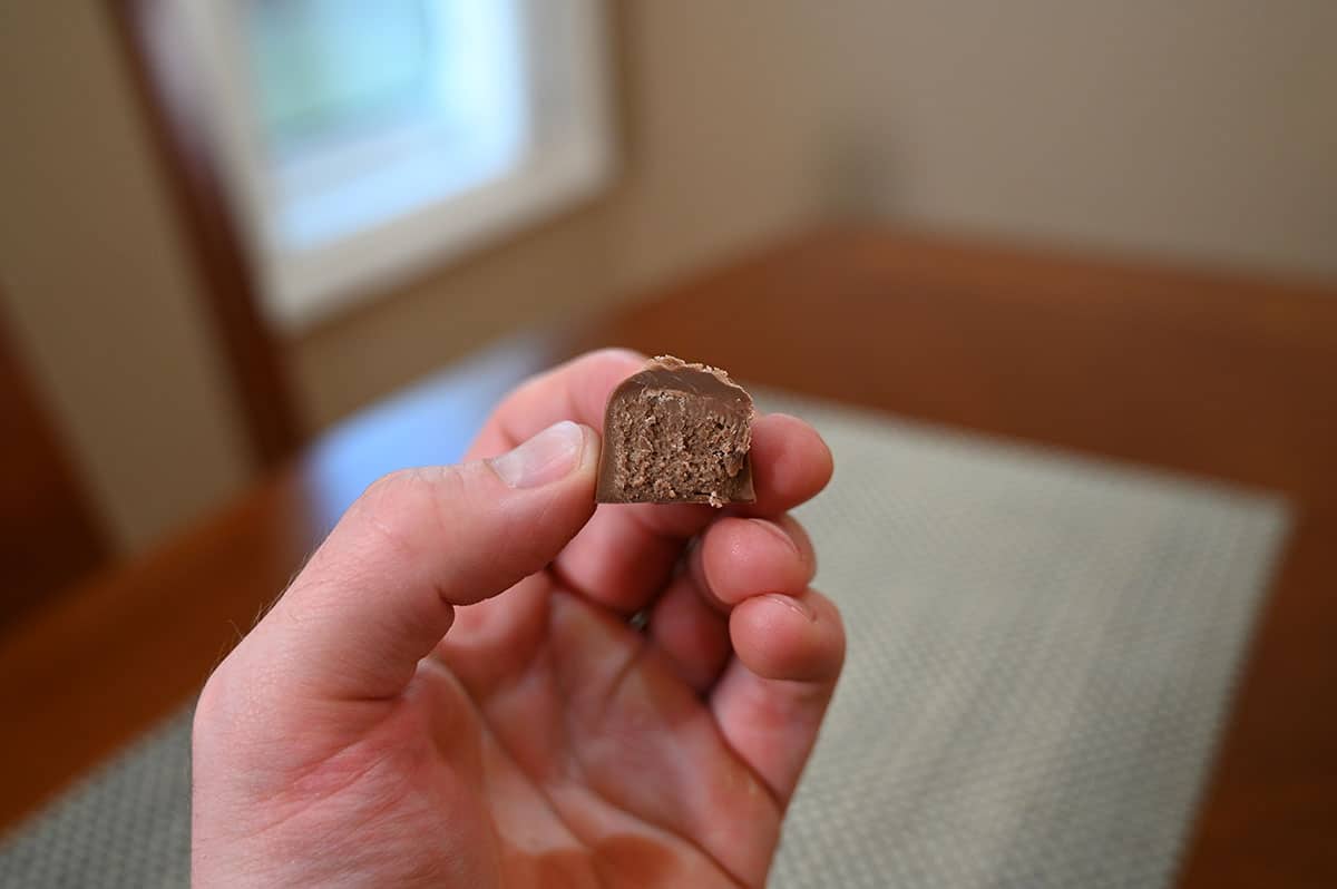 Closeup image of a hand holding a mint milk chocolate truffle with a bite taken out of it so you can see the center.