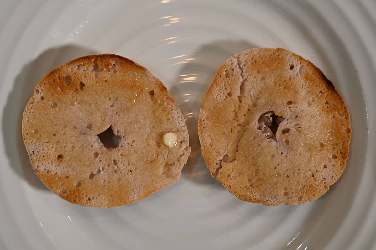 Image of the bagel cut in half toasted with butter served on a white plate.