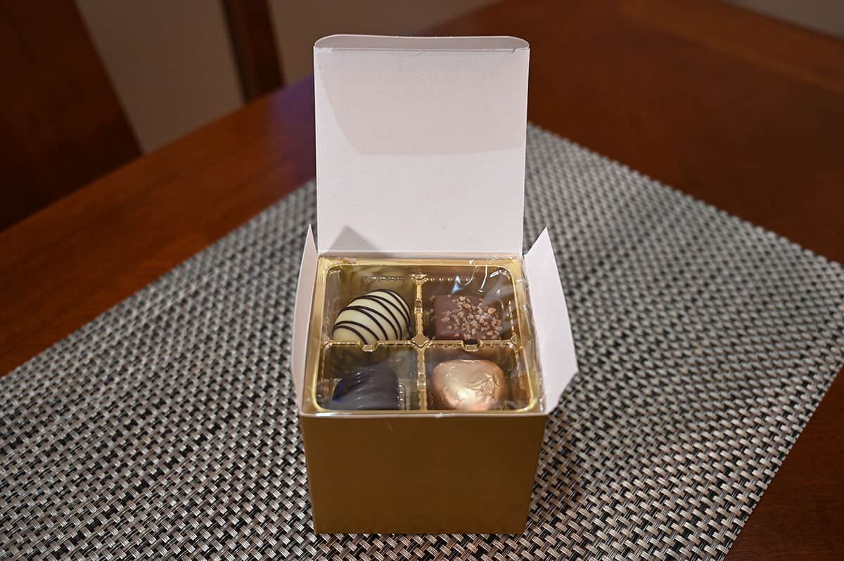 Image of one box of chocolates open and sitting on a table so you can see the tray inside the box and the chocolates sitting inside the tray. 