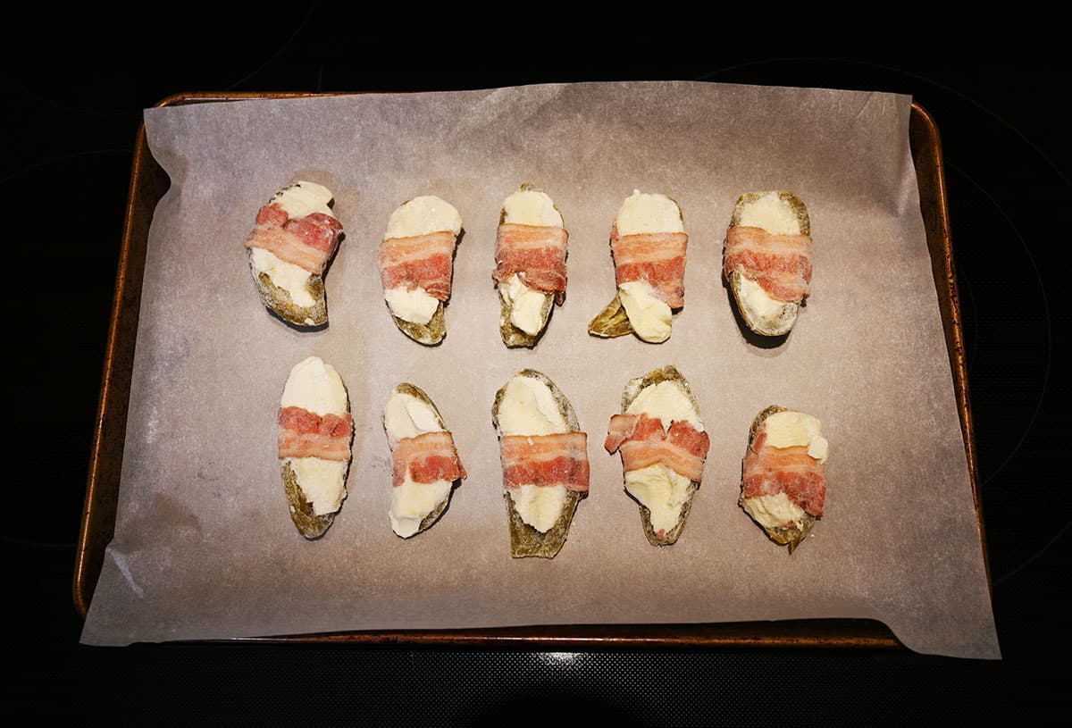 Image of the frozen bacon wrapped jalapenos on a cookie sheet lined with parchment paper prior to cooking them in the oven.