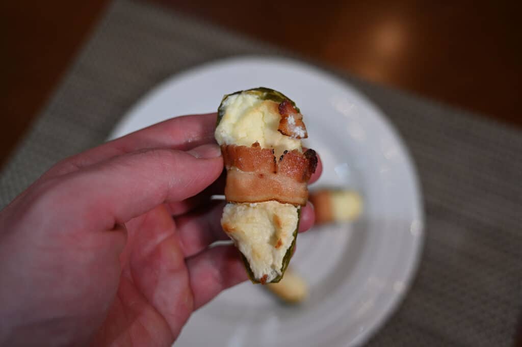 Closeup image of a hand holding one bacon wrapped jalapeno after being cooked.