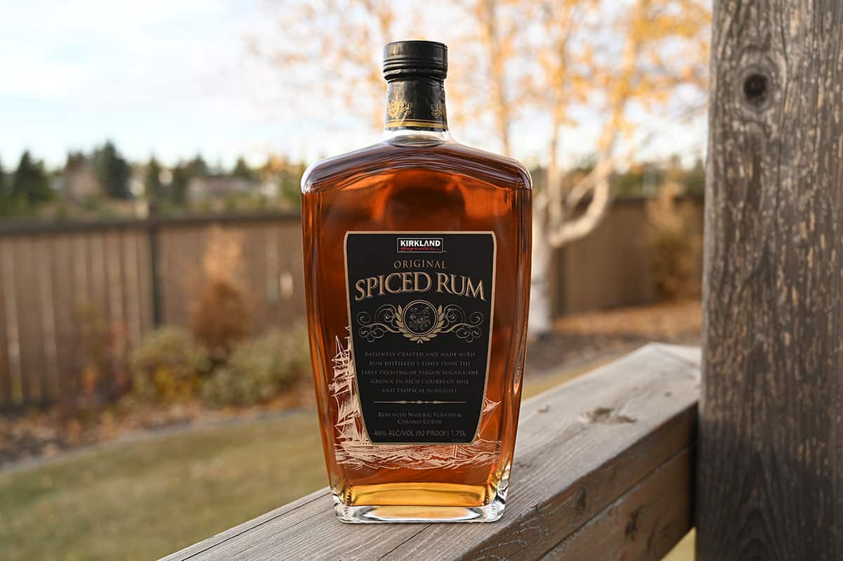 Image of the Costco Kirkland Signature Original Spiced Rum bottle sitting on a deck outside with trees in the background.