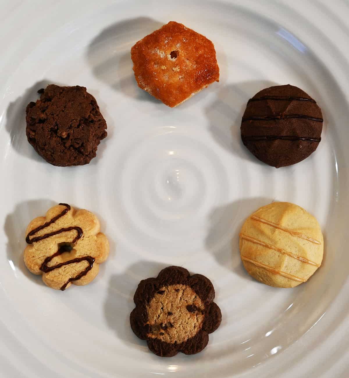 The six different kinds of cookies served on a white plate in a circle, closeup image showing what each cookie looks like.