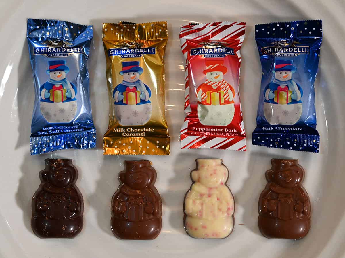 Image of all four different kinds of snowmen served on a white plate with the corresponding wrapper above them. Dark chocolate sea salt caramel, milk caramel, peppermint bark and milk chocolate.