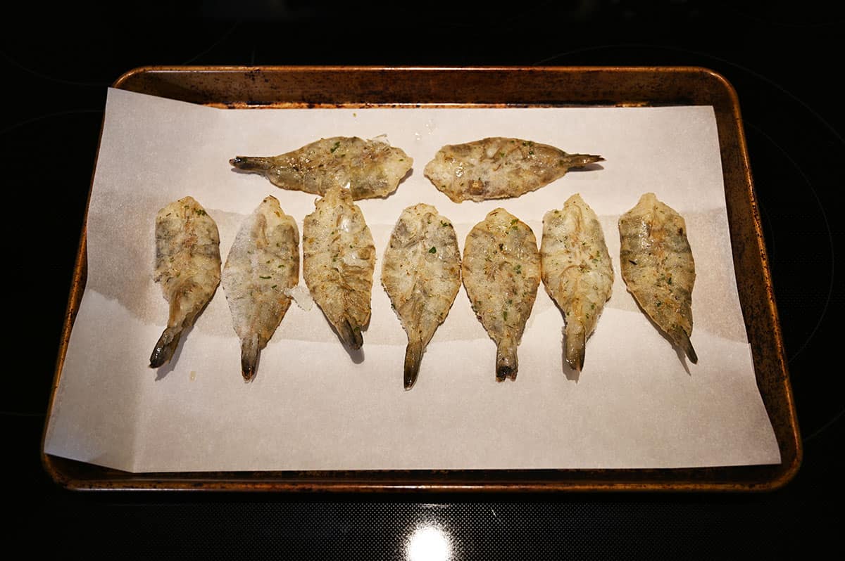 Image showing raw shrimp on a baking tray lined with parchment paper sitting on a stovetop.