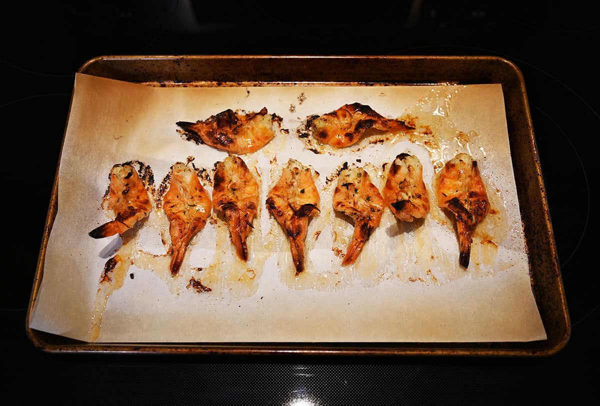 Image showing the cooked shrimp on a baking tray lined with parchment paper sitting on a stovetop.