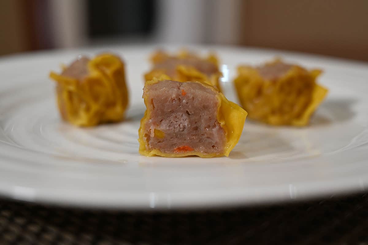 Side view image of five dumplings cooked and served on a white plate, one dumpling is cut in half so you can see the filling.