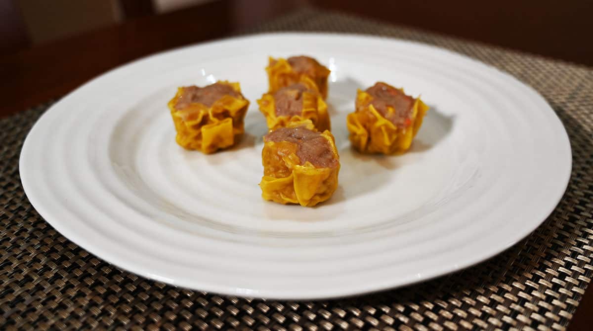 Side view image of five dumplings cooked and served on a white plate.