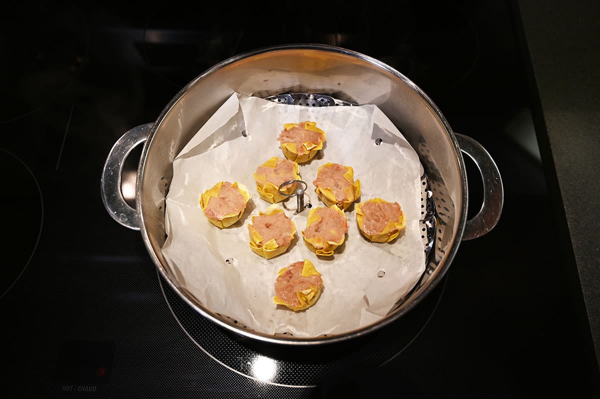 Top down image of a pot with a steamer tray on a stove top with the dumplings ready to be cooked.