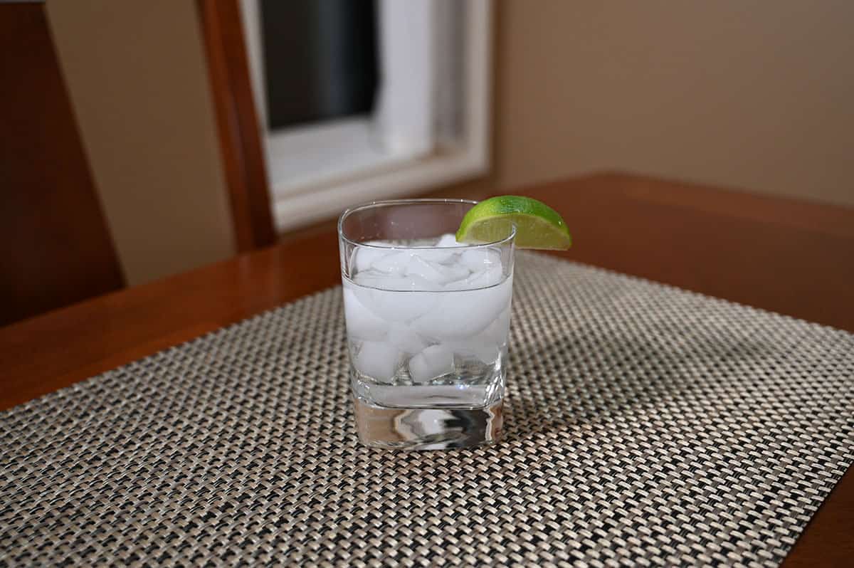 Image of a glass of gin and soda with a lime wedge served on a table.