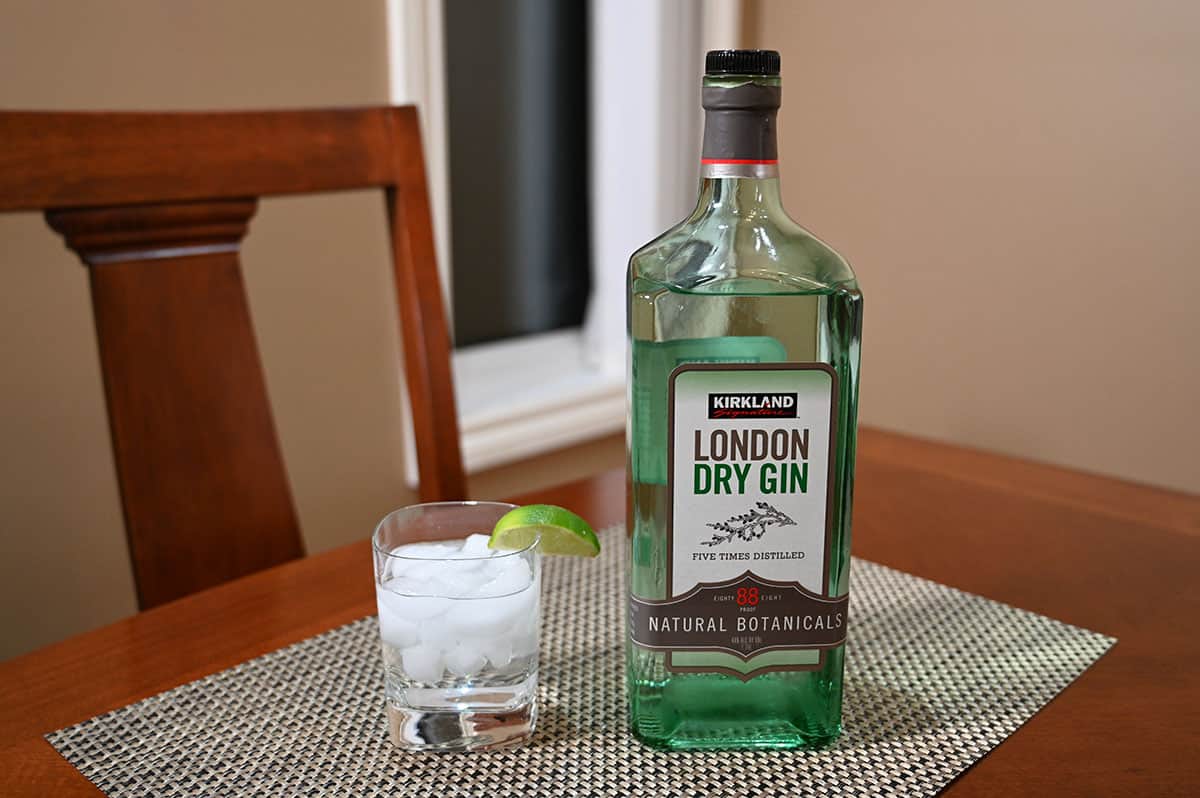 Image of the bottle of Kirkland Signature gin beside a prepared gin and soda with a lime wedge. Sitting on a table.