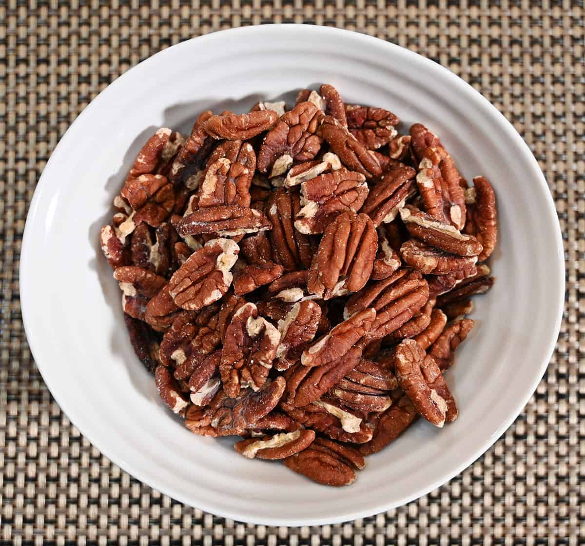 Top down image of a white bowl full of pecans.