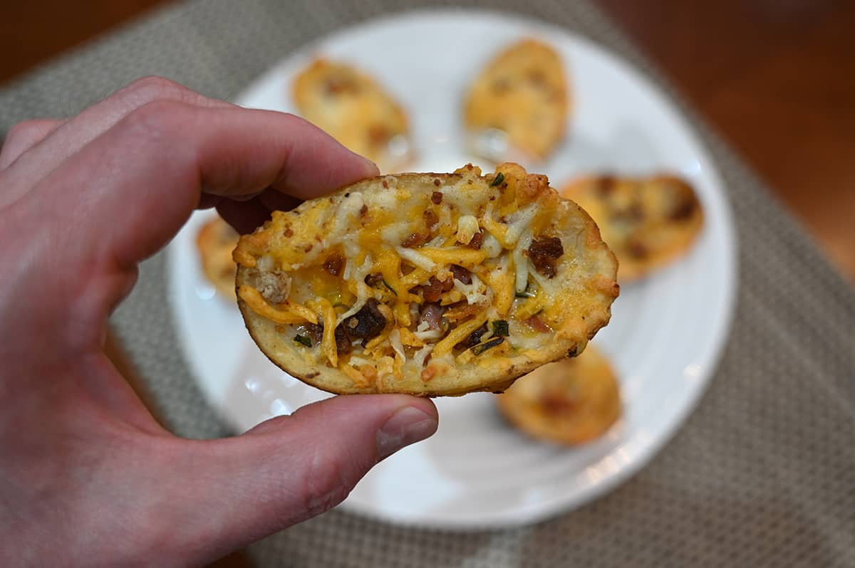 Closeup image of a hand holding one potato skin close to the camera with a plate of potato skins in the background.