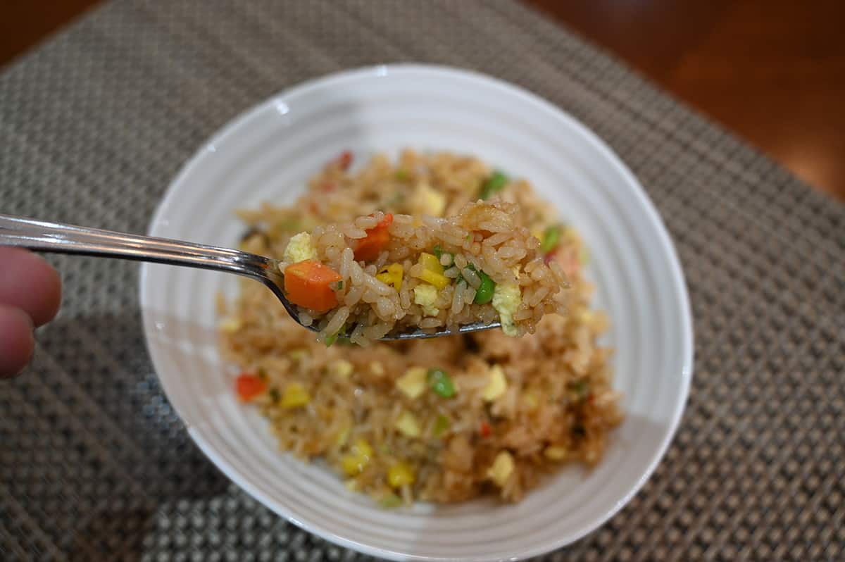 Top down image of a forkful of fried rice with a bowl of the vegetable fried rice in the background behind it.