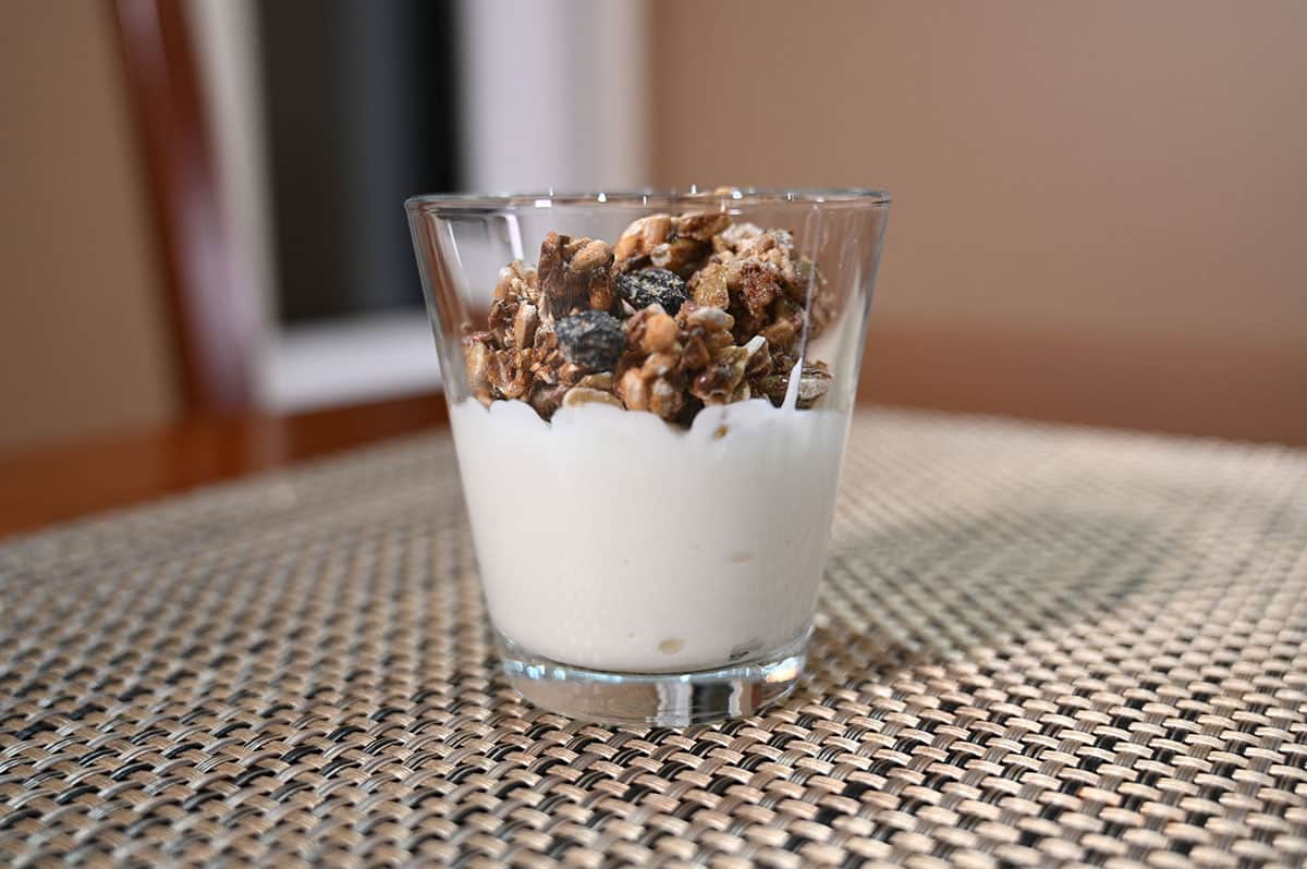 Closeup image of a glass cup with yogurt and the granola sprinkled on top. 