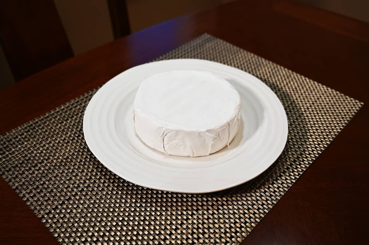 Image of the brie with the rind on sitting on a white plate on the table. 