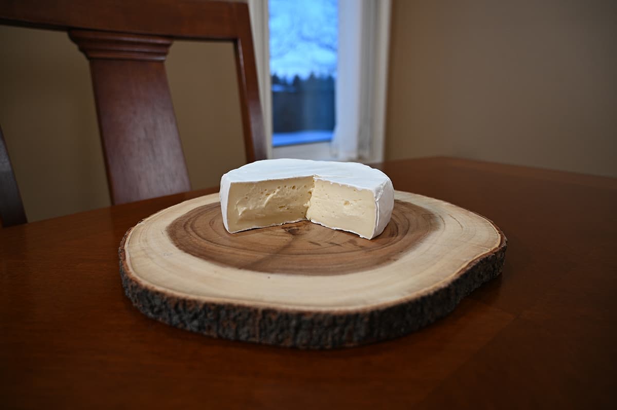 Image of the brie served on a charcuterie board with a wedge sliced out of it.