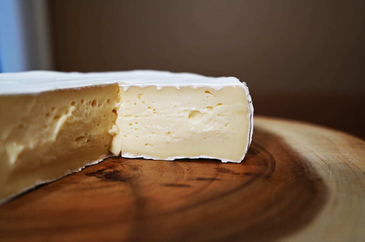 Closeup image of the inside of the brie with a piece cut out so you can see what the brie looks like under the rind.