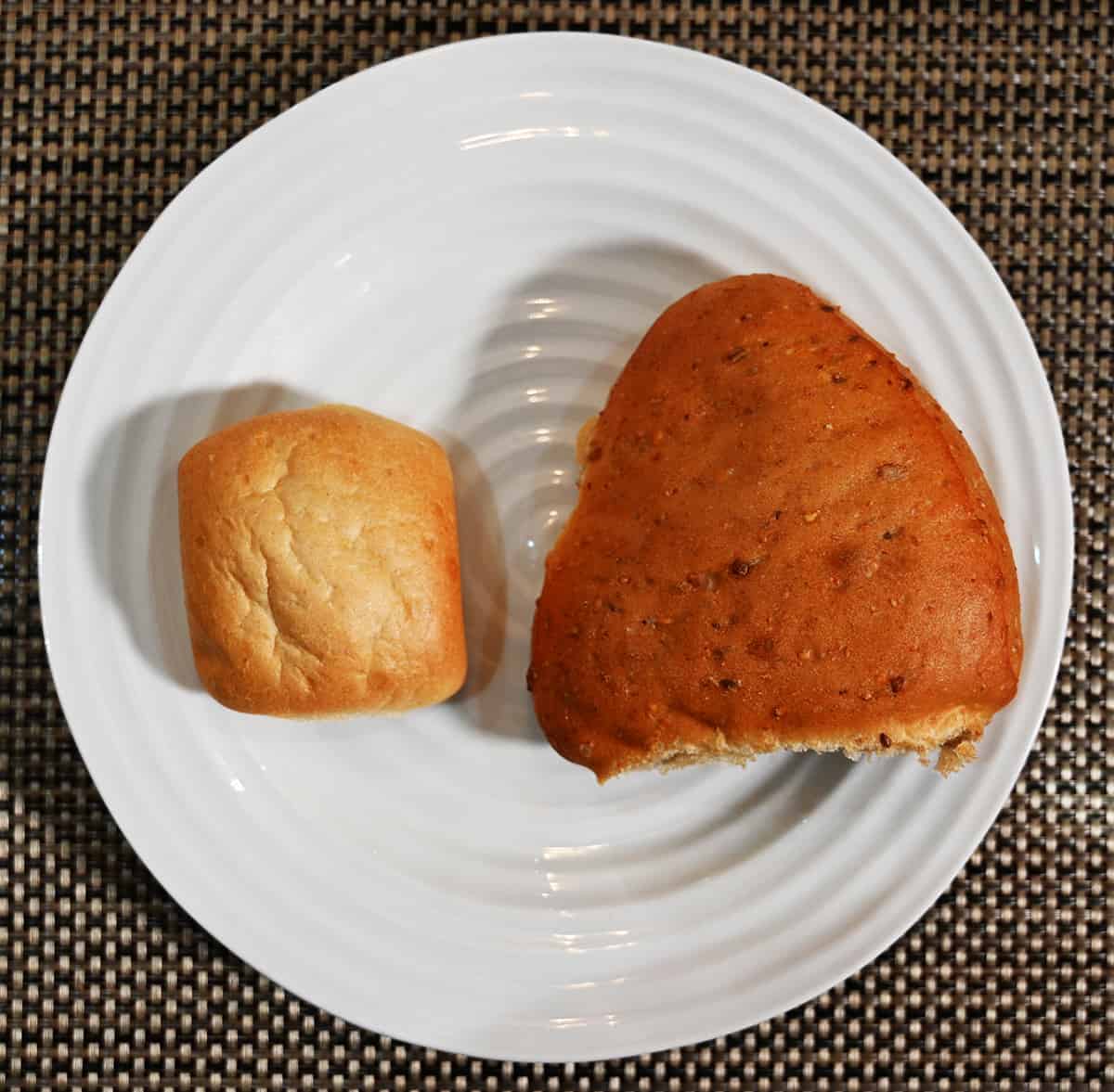 Top down image of one Italian ciabatta bun on a white plate beside one 9 grain ciabatta bun.