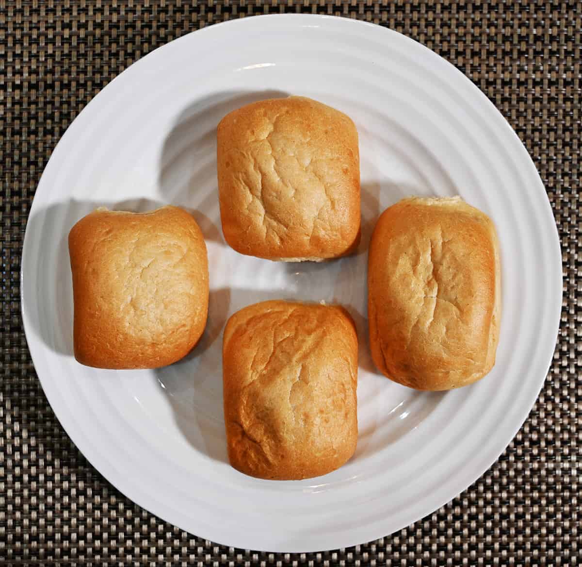 Top down image of four Italian ciabatta buns sitting on a white plate.