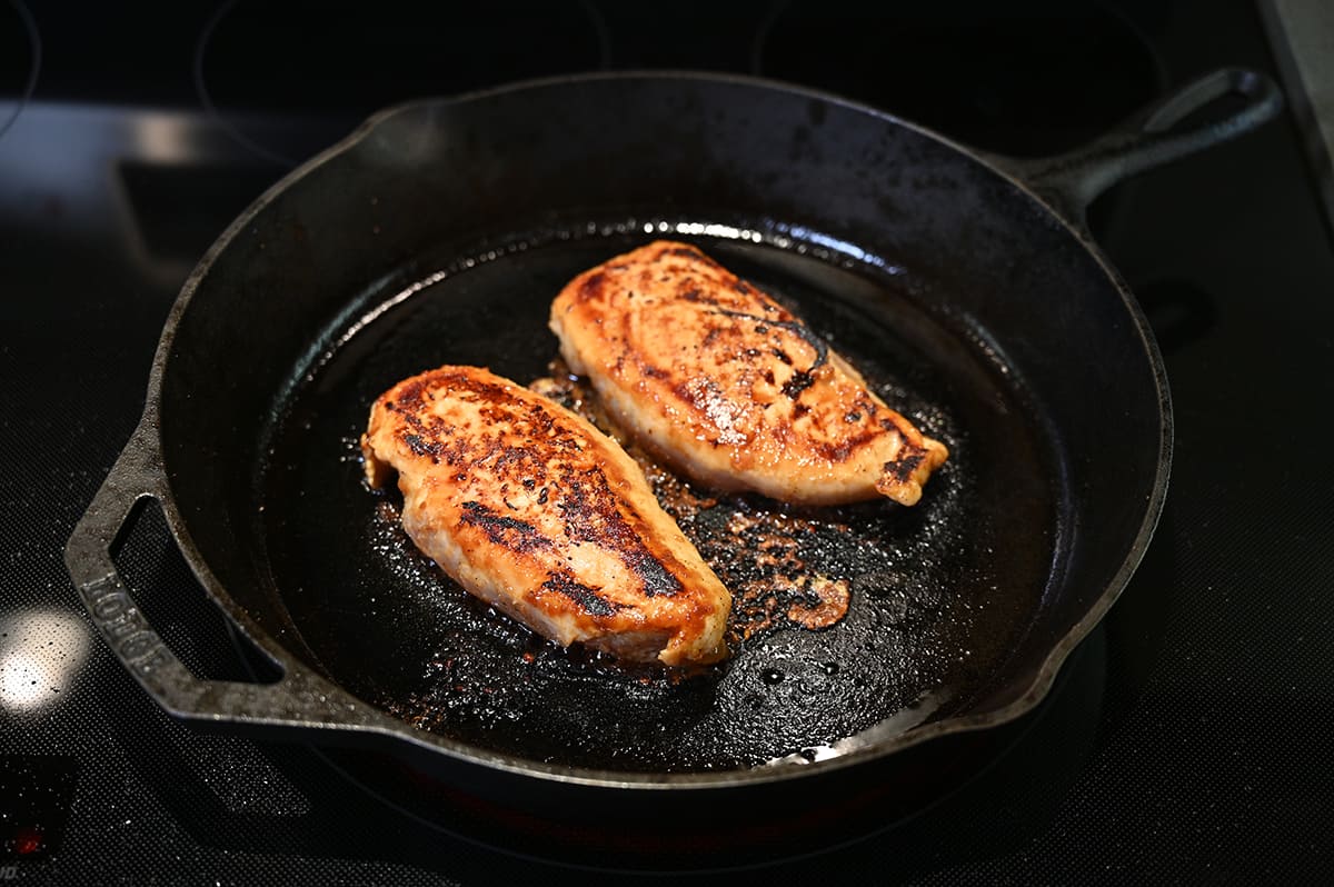 Image of two chicken breasts being cooked in a cast iron skillet.