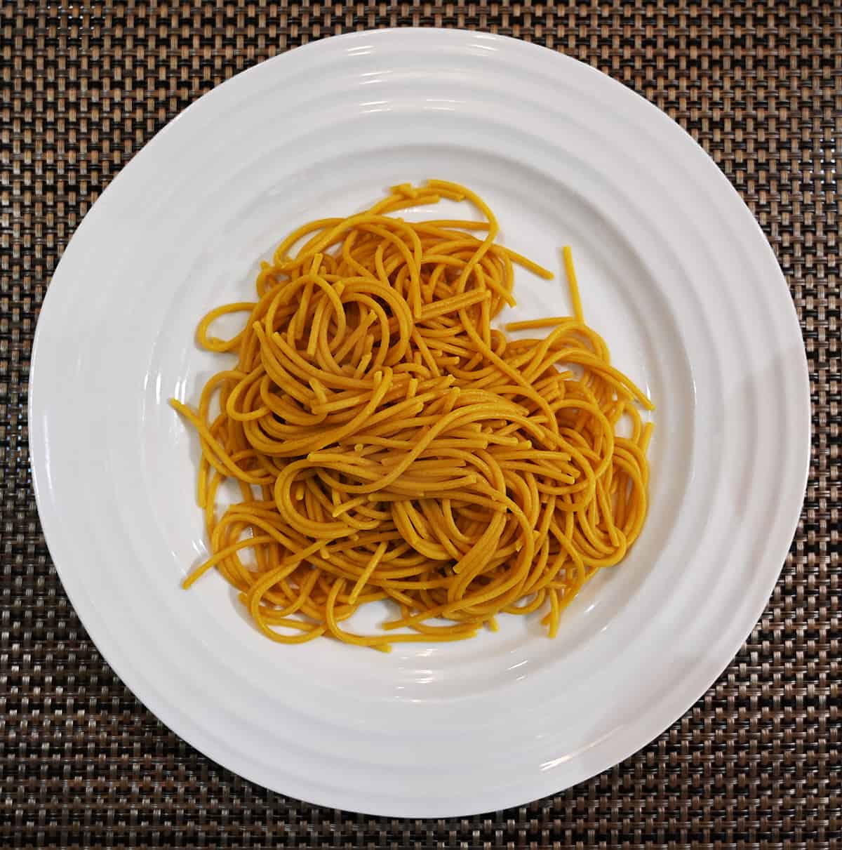 Top down image of cooked spaghetti on a white plate without any sauce on it.