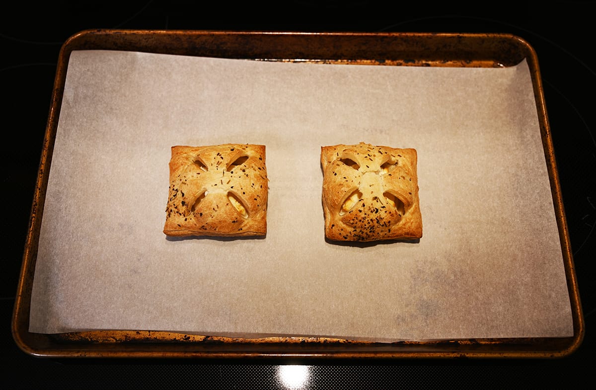 Top down image of a baking tray lined with parchment paper with two baked pastries on it.