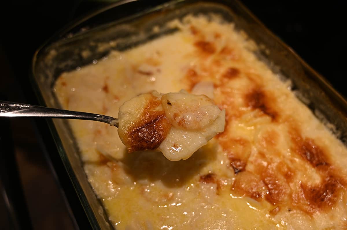 Image of spoon serving the potatoes au gratin from the casserole dish showcasing how soupy the potatoes are.