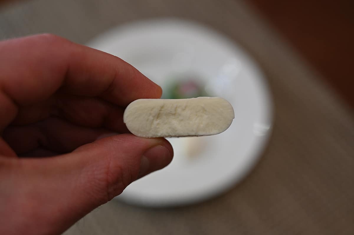 Closeup image of a hand holding one plant-based Babybel with a bite taken out of it so you can see the middle.