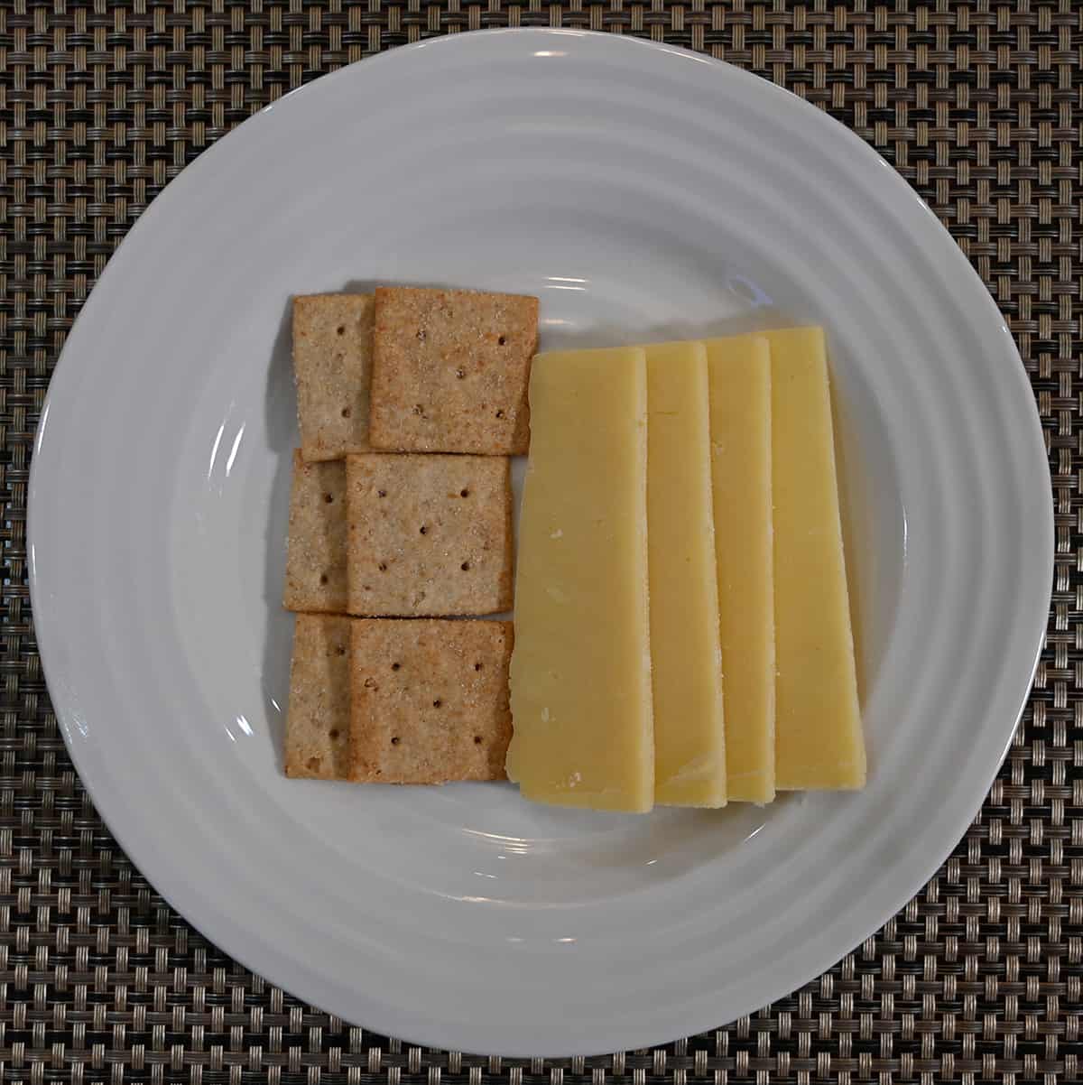 Top down image of the Dubliner cheese sliced and served with crackers on a white plate.