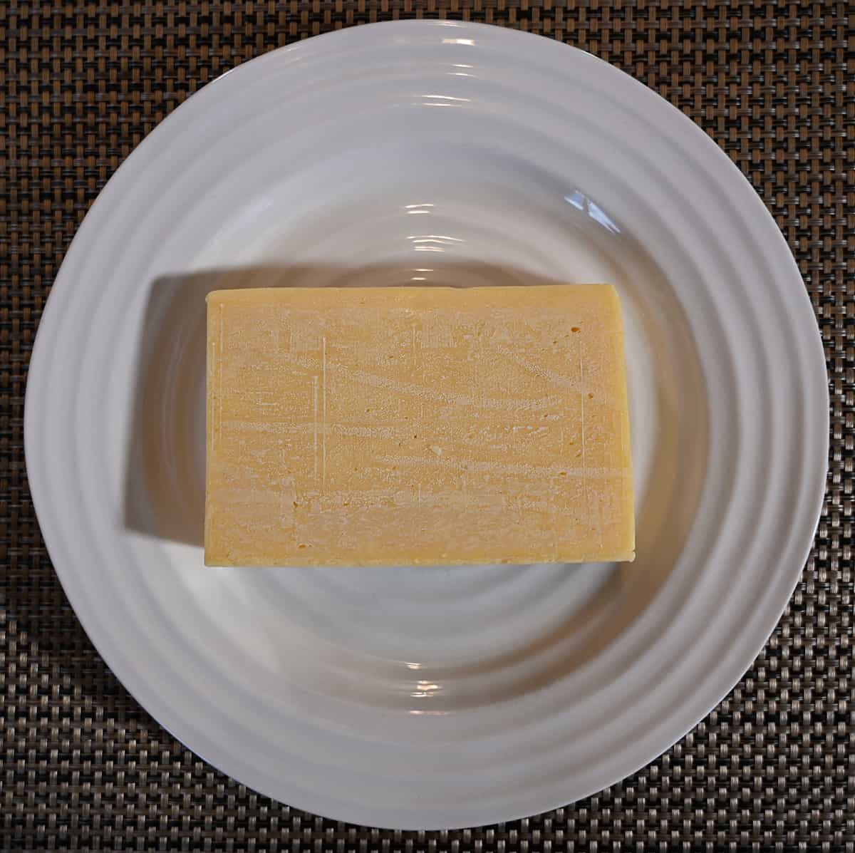Top down image of the entire block of cheese unwrapped and on a white plate.