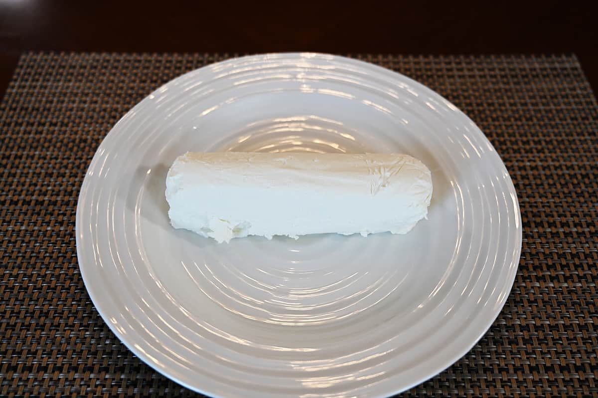 Image of one entire goat cheese roll served on a white plate. Side view image.