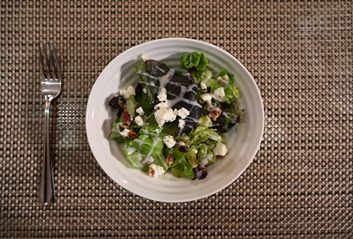 Top down image of a salad prepared with the goat cheese and a drizzle of dressing on top. Served in a white bowl with a fork beside the bowl.