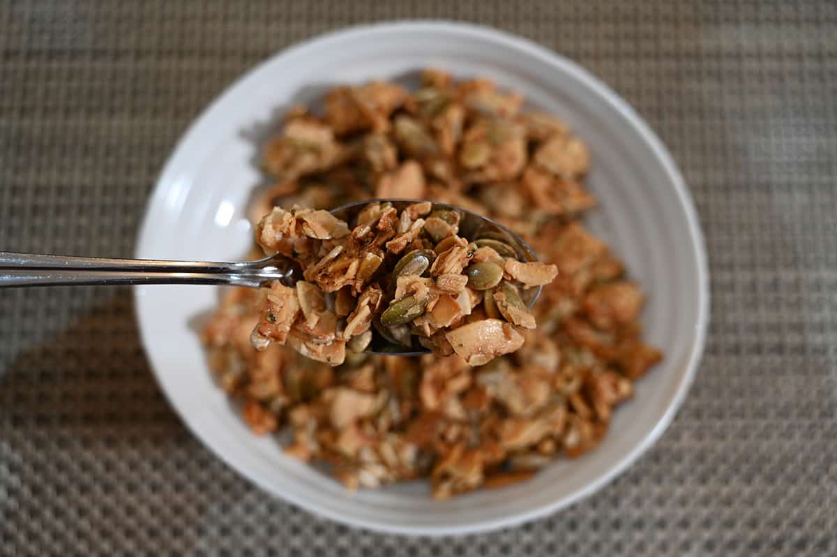 Closeup image of a spoon full of coconut clusters with a bowl of clusters in the background.