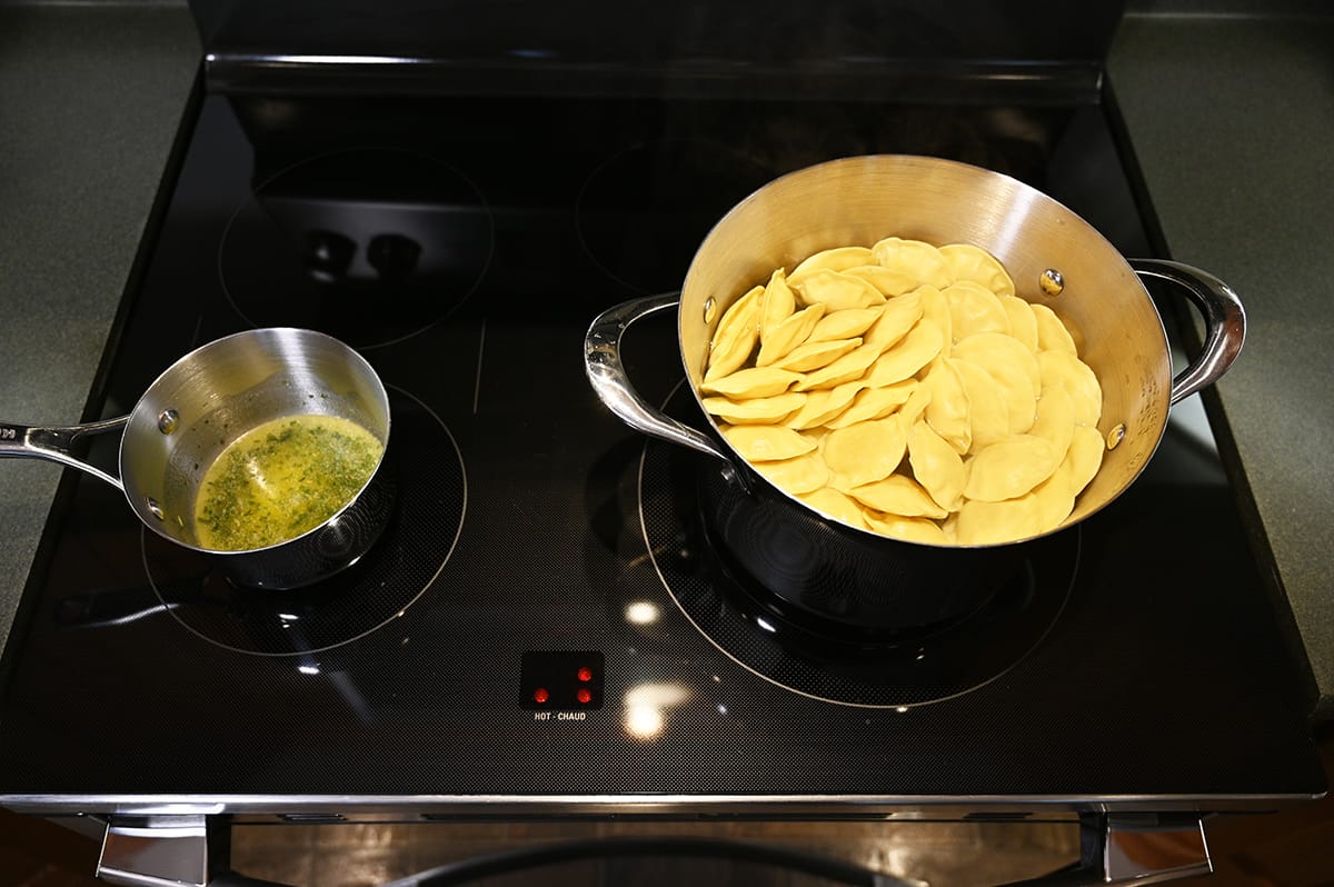 Top down image of a pot of ravioli prepared and a saucepan full of butter sauce on a burner.