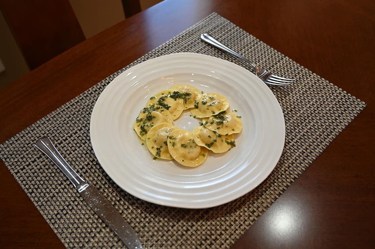 Image of eight ravioli served on a white plate in a circle with a garlic butter sauce and parsley sprinkled on top.