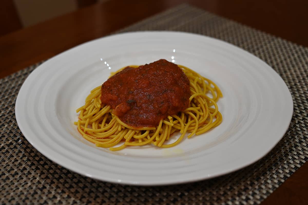 Side view image of a white plate with prepared spaghetti with sauce on top.