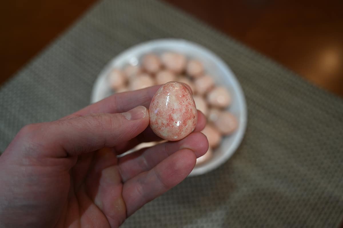 Closeup image of a hand holding one chocolate in front of the care with a bowl full of chocolates in the background.