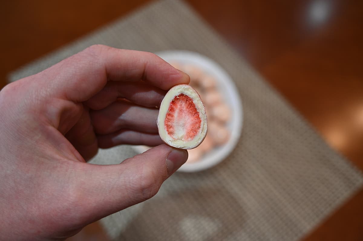 Closeup image of a hand holding one chocolate  in front of the camera cut in half so you can see the strawberry inside.