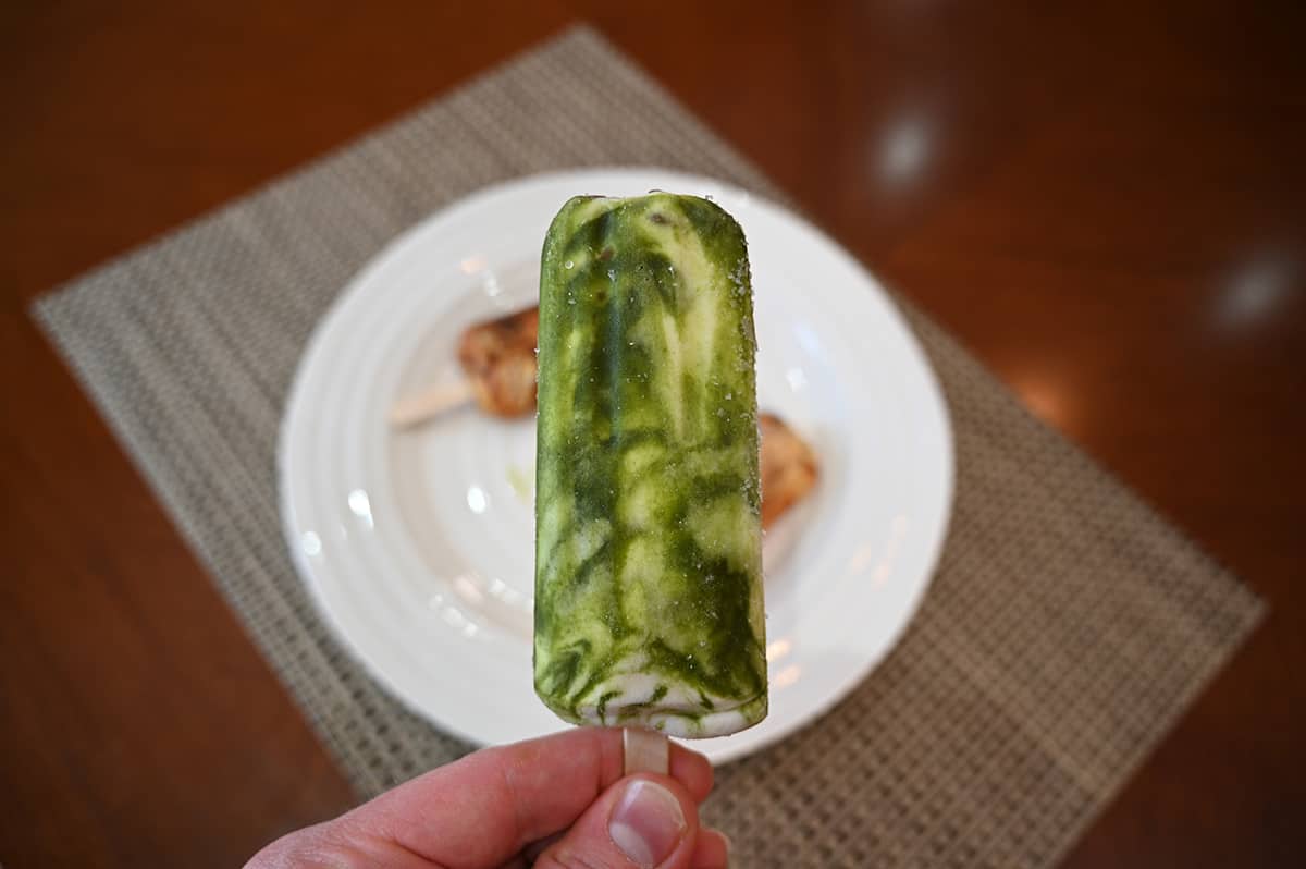 Image of a hand holding a matcha latte frozen dessert bar near the camera.