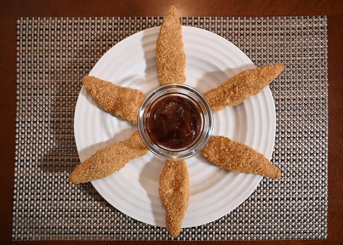 Top down image of a plate of chicken strips plated in a circular fashion with a bowl of dip in the center.