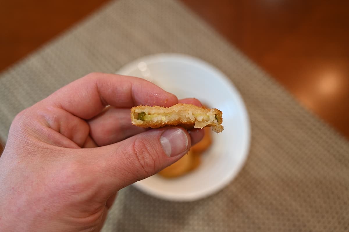 Image of a hand holding one dill pickle chip with a bite taken out of it so you can see the inside.