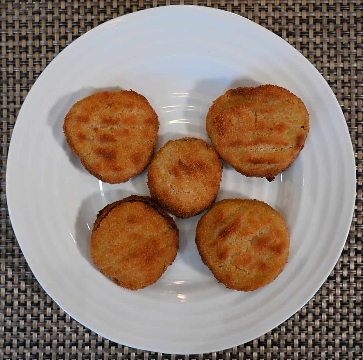 Top down of five cooked breaded dill pickle chips on a white plate.