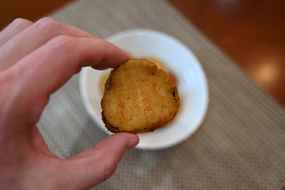 Closeup image of a hand holding one cooked dill pickle chip close to a camera.